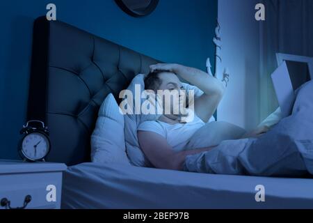 Ein übermütiger Mann arbeitet spät in der Nacht an seinem Laptop Stockfoto