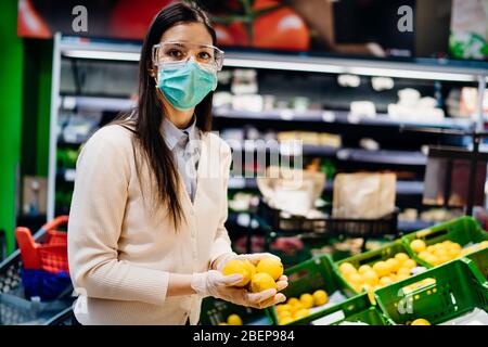Frau mit Schutzmaske Kauf im Supermarkt für frische Produkte, Budget-Einkauf für Zitrusfrüchte während der Pandemie.natürliche Quelle von Vitami Stockfoto