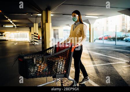 Frau, die Maske Lebensmittel / Lieferungen Einkaufen im Supermarkt, schieben Trolley.Food Lieferungen Mangel.Panik Kauf und horten.Empty Parkhaus.Su Stockfoto