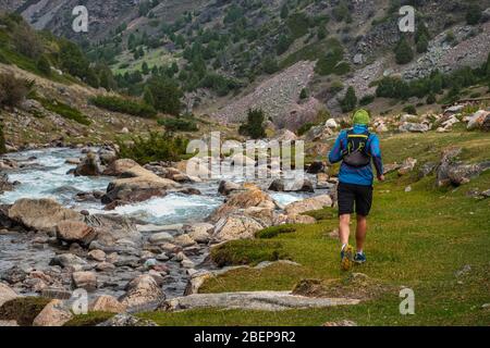 Runner Kerl joggt im Hochland. Athlet läuft in der Nähe eines Gebirgsflusses. Der Mann trainiert im Freien. Trail Running Stockfoto