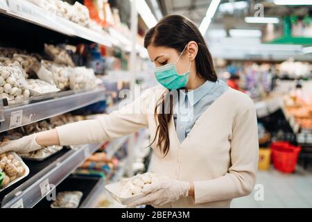 Frau mit Maske sicher einkaufen für Lebensmittel inmitten der Coronavirus-Pandemie in einem sortierten Lebensmittelgeschäft.COVID-19 Lebensmittel im Supermarkt kaufen.Panik kaufen Stockfoto