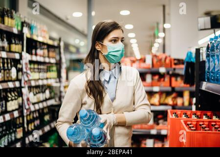 Frau mit Maske sicher einkaufen für Lebensmittel inmitten der Coronavirus-Pandemie in einem sortierten Lebensmittelgeschäft.COVID-19 Lebensmittel im Supermarkt kaufen.Panik kaufen Stockfoto