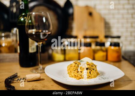 Gelbes Kurkuma-Risotto mit wilden Steinpilzen Platte mit Rotwein serviert.Safranreis mit Parmesan-Käse.Italienische traditionelle Rezepte mit Wein Stockfoto