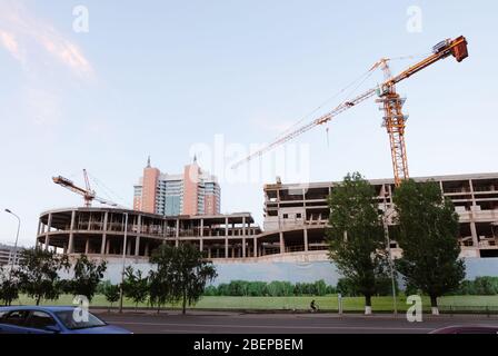 NUR-SULTAN, ASTANA, KASACHSTAN - 3. JUNI 2015: Zwei gelbe Kränen auf einem neuen Gebäude mit Blick auf die Stadt und Bäume um die Zeit des Sonnenuntergangs Stockfoto