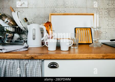 Detail der kleinen Küche.Weiße Schränke mit Holzmetzern Block counter top.Two Tassen in der Küche mit Glaswaren und Geschirr.Tiny Haus Küche fo Stockfoto