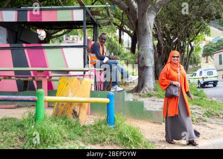 Eine hell gekleidete muslimische Frau spaziert im Bo Kaap Bezirk von Kapstadt. Bo-Kaap ist bekannt für seine farbenfrohen Häuser und gepflasterten Straßen. Die Gegend ist traditionell ein multikulturelles Viertel, und 56.9% der Bevölkerung identifizieren sich als Muslime. Nach Angaben der South African Heritage Resources Agency enthält das Gebiet die größte Konzentration von Architektur aus der Zeit vor 1850 in Südafrika und ist das älteste noch erhaltene Wohnviertel in Kapstadt. Stockfoto