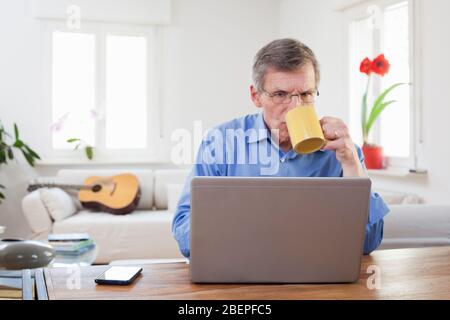 Ältere oder ältere Geschäftsmann trinken Kaffee vor einem Computer in seinem Home Office - konzentrieren Sie sich auf die Kante des Laptops Stockfoto