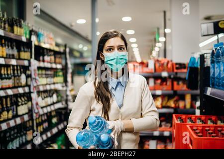 Frau mit Maske sicher einkaufen für Lebensmittel inmitten der Coronavirus-Pandemie in einem sortierten Lebensmittelgeschäft.COVID-19 Lebensmittel im Supermarkt kaufen.Panik kaufen Stockfoto