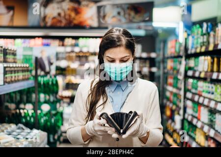 Besorgte Frau mit Maske Lebensmittel einkaufen im Supermarkt Blick auf leere Brieftasche.nicht genug Geld, um Lebensmittel zu kaufen.Covid-19 Quarantäne sperren.Financial Stockfoto