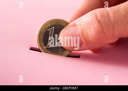 Hand, die eine Euro-Münze in eine Geldbox auf rosa Hintergrund legt Stockfoto
