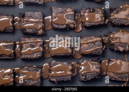 Schokoladenkuchen Brownie Quadrate mit Schokolade Ganache Sauce auf schwarzem Hintergrund isoliert tropften Stockfoto