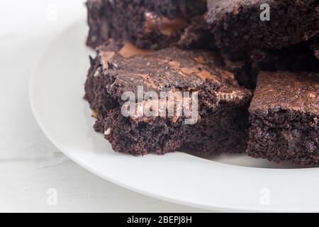 Schokoladenbrownies mit geschmolzenen Schokoladenstückchen in einem weißen Teller auf weißem rustikalem Hintergrund gestapelt Nahaufnahme mit Platz für Text Stockfoto
