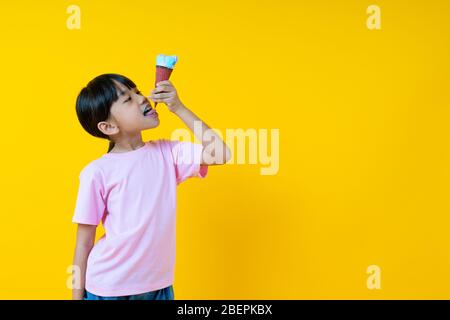 Porträt von jungen asiatischen Mädchen Eis essen, Thai hübsche Kind lecken unten von Kegel auf gelbem Hintergrund Stockfoto