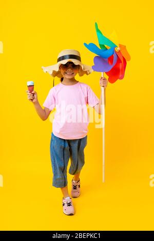 Porträt von jungen asiatischen hübschen Mädchen zu Fuß und hält bunte Turbine und Eis, Thai Kind im Sommer-Stil auf gelbem Hintergrund Stockfoto