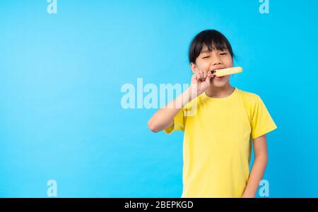 Junge asiatische Mädchen Kind essen Eis und Posting lustig auf blauem Hintergrund im Studio Stockfoto