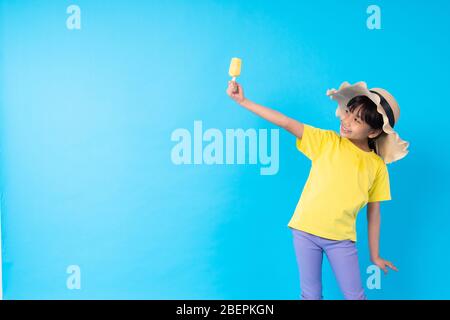 Junge asiatische Mädchen Kind essen Eis und Posting lustig auf blauem Hintergrund im Studio Stockfoto