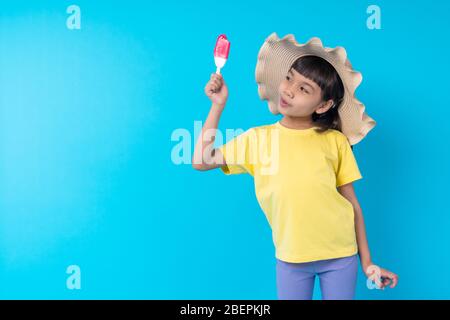 Junge asiatische Mädchen Kind essen Eis und Posting lustig auf blauem Hintergrund im Studio Stockfoto