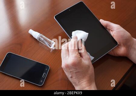 Ein Mann, der Tablet-Bildschirm und Mobiltelefon mit weichem Tuch reinigt. Coronavirus Prävention und Desinfektion zu Hause. Stockfoto