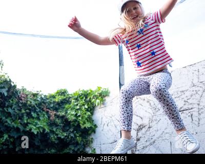 Ein vierjähriges Mädchen springt auf einem Trampolin in ihrem Stadtgarten in London, Großbritannien Stockfoto