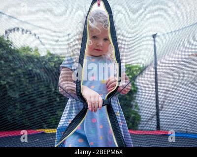 Ein zweijähriges Mädchen (fast drei) am Eingang zu ihrem Gartentrampolin. Stockfoto