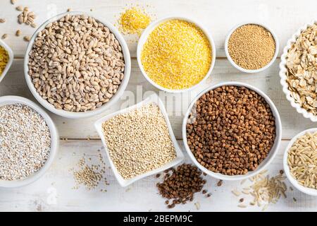 Auswahl von Vollkornprodukten in weißen Schalen - Reis, Hafer, Buchweizen, Bulgur, Haferbrei, Gerste, Quinoa, Amaranth, Stockfoto