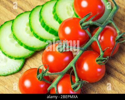 Vittoria Kirschtomaten auf der Rebe mit Gurkenscheiben auf einem Holzhackbrett Stockfoto