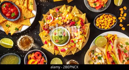 Mexikanisches Speisepanorama, aufgenommen von oben auf schwarzem Hintergrund. Nachos, Guacamole, Tequila, Tacos etc., eine flache Lage Stockfoto