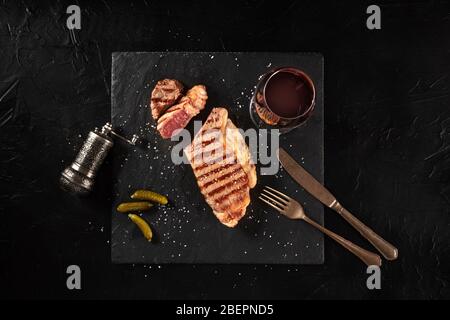 Gegrilltes Rindersteak mit Rotwein, mittelselten, von oben auf schwarzem Hintergrund geschossen Stockfoto