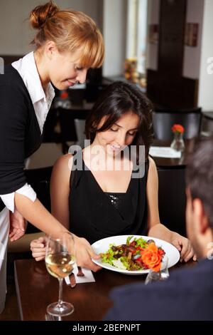 Kellnerin im Restaurant serviert einer Frau einen Salat Stockfoto