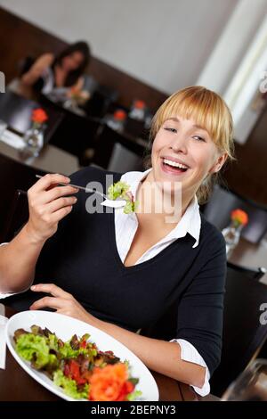 Lachende Frau mit Salat auf der Gabel im Restaurant Stockfoto