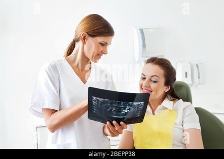 Zahnarzt zeigt ein Röntgenbild eines Patienten auf dem Zahnstuhl Stockfoto