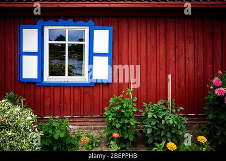 Fenster mit offenen Holzfenstern an einer roten Wand mit Blumengarten darunter Stockfoto