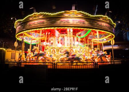 Ein klassisches Karussell, das nachts dreht und lebendige und bunte Lichtwege in London, Großbritannien, hinterlässt Stockfoto