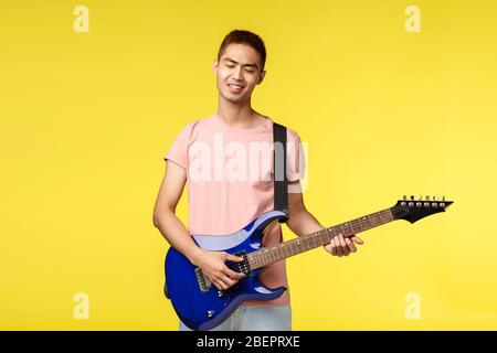 Lifestyle, Freizeit und Jugendkonzept. Sorglos gut aussehende asiatische Mann in rosa T-Shirt schließen die Augen und lächeln, erfreut wie E-Gitarre spielen, genießen Stockfoto