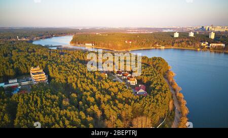 Erholungszone und große Stadt Luftaufnahme. Flussufer mit Wald und Sanatorium im Frühling Sonnenlicht. Der Aprilabend am See neben Minsk, Weißrussland. Beau Stockfoto