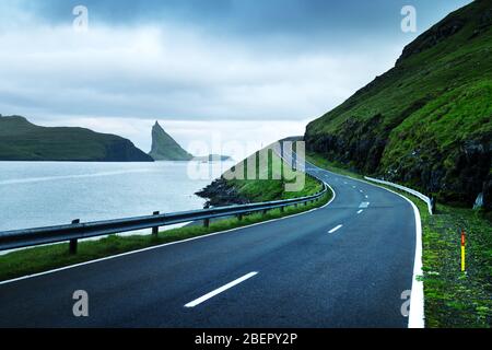 Dramatische Abendlicher Blick von der Straße und der Drangarnir und Tindholmur Felsen im Hintergrund auf der Insel Vagar, Färöer, Dänemark Stockfoto