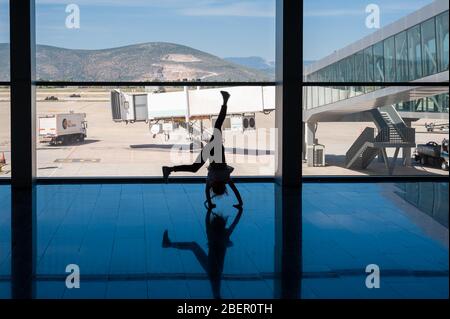 05/26/2019. Flughafen Bodrum / Flughafen Milas Mugla. Türkei. Kleines Mädchen, das Kart-Räder macht, übt aus Langeweile, während es auf ihren Flug wartet. Stockfoto