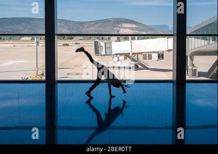 05/26/2019. Flughafen Bodrum / Flughafen Milas Mugla. Türkei. Kleines Mädchen, das Kart-Räder macht, übt aus Langeweile, während es auf ihren Flug wartet. Stockfoto