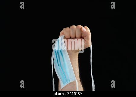 Faust, die eine Maske im Symbol des Kampfes gegen Coronavirus auf schwarzem Hintergrund Stockfoto