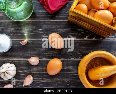 Knoblauchköpfe, Eier, Salz und Öl verteilt, um die für spanische Lebensmittel typische Ajoaceite-Sauce in einem Monat abgetragenem und altem schwarzen Holz vorzubereiten Stockfoto