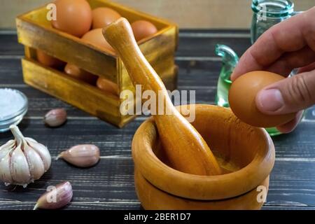 Knoblauchköpfe, Eier, Salz und Öl verteilt, um die für spanische Lebensmittel typische Ajoaceite-Sauce in einem Monat abgetragenem und altem schwarzen Holz vorzubereiten Stockfoto
