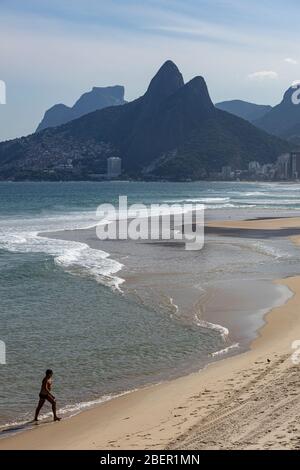 Silhouette einer Person am Strand von Ipanema mit dem Berg der zwei Brüder während des COVID-19 Virus Ausbruch in Rio de Janeiro nach einer großen Gezeiten Stockfoto