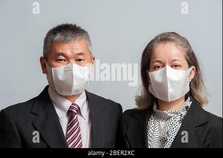 Vorderansicht des asiatischen Paares mittleren Alters in formeller Kleidung mit weißer 3D-Einweg-Gesichtsmaske zum Schutz vor neuartigem Coronavirus (COVID-19). Stockfoto