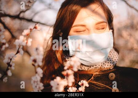 Porträt von glücklichen Teenager-Mädchen mit Gesicht medizinische Maske stehend von blühenden Baum im Frühjahr Stockfoto