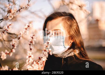 Junge Frau mit Gesicht medizinische Maske riechenden Blumen im Frühjahr Stockfoto