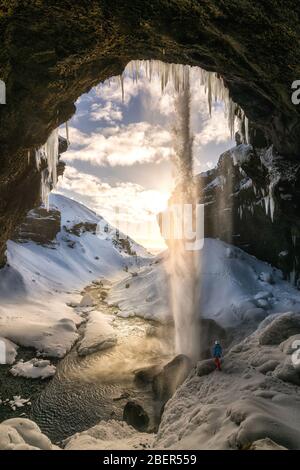 Spektakulärer Wasserfall in Island mit Kerl Blick auf ihn bei Sonnenuntergang Zeit mit Wasser fließt durch Decke alle Schnee bedeckt Stockfoto