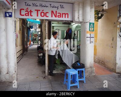 Vietnamesischer lokaler Barber, der seinen Kunden in seinem Barbers-Geschäft in einer Straße in Hanoi, Vietnam 2020 Haare schneidet Stockfoto