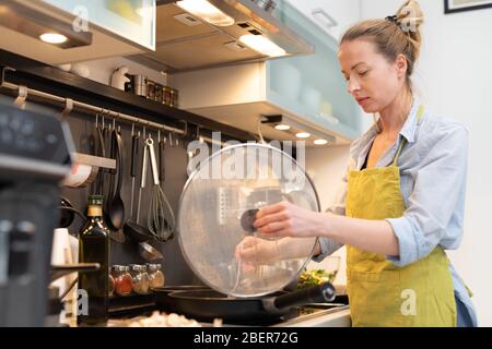 Übernachten Sie zu Hause Hausfrau Frau, die in der Küche kocht, rühren Sie Frittiergericht in einem Topf, und bereiten Sie Essen für das Familienessen zu. Stockfoto