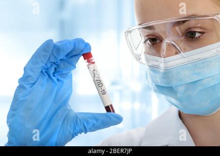 Junge Frau in Schutzkleidung, die das Blutprobenrohr auf COVID-19 im medizinischen Labor testet Stockfoto