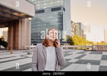 Glückliche junge Geschäftsfrau in formeller Kleidung im Gespräch über Smartphone Stockfoto